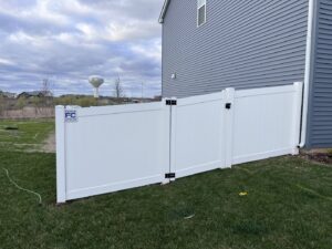 A newly installed white vinyl privacy fence with a gate next to a residential home by Fence Connection, Inc. in Elgin, IL.