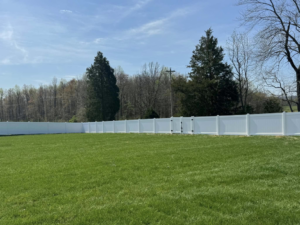 A newly installed white vinyl privacy fence with a gate enclosing a large yard by KY Fencing Unlimited in Louisville, KY.