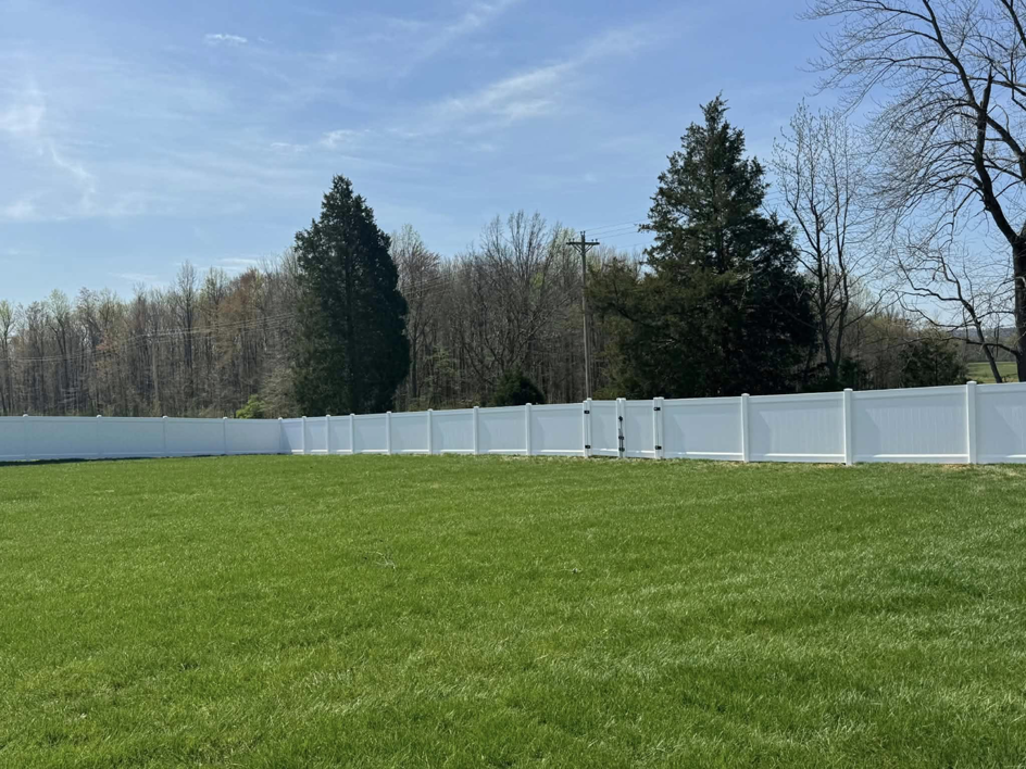 A newly installed white vinyl privacy fence with a gate enclosing a large yard by KY Fencing Unlimited in Louisville, KY.