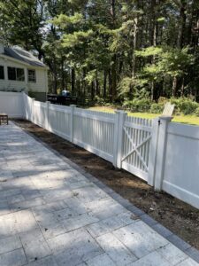 A newly installed white vinyl privacy fence with a gate next to a patio by OMA Fence,LLC in Weymouth, MA