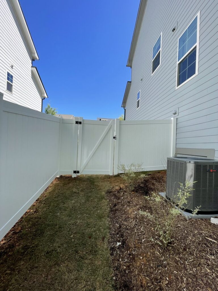 A white vinyl privacy fence with a gate installed between two residential homes by RDU Fence in Holly Springs, NC.