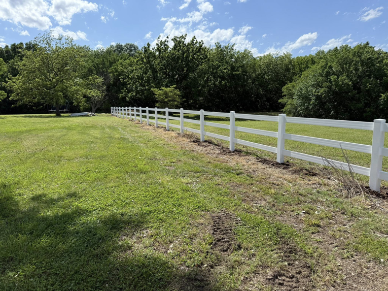 A long white vinyl ranch-style fence installed in a grassy field by NC Fencing LLC in Wichita, KS.