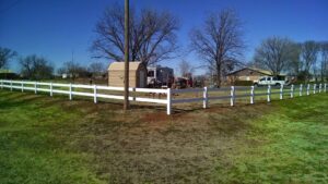 A long white vinyl ranch-style fence installed in a grassy field by Pro Insulation and Fence in Wichita Falls, TX.