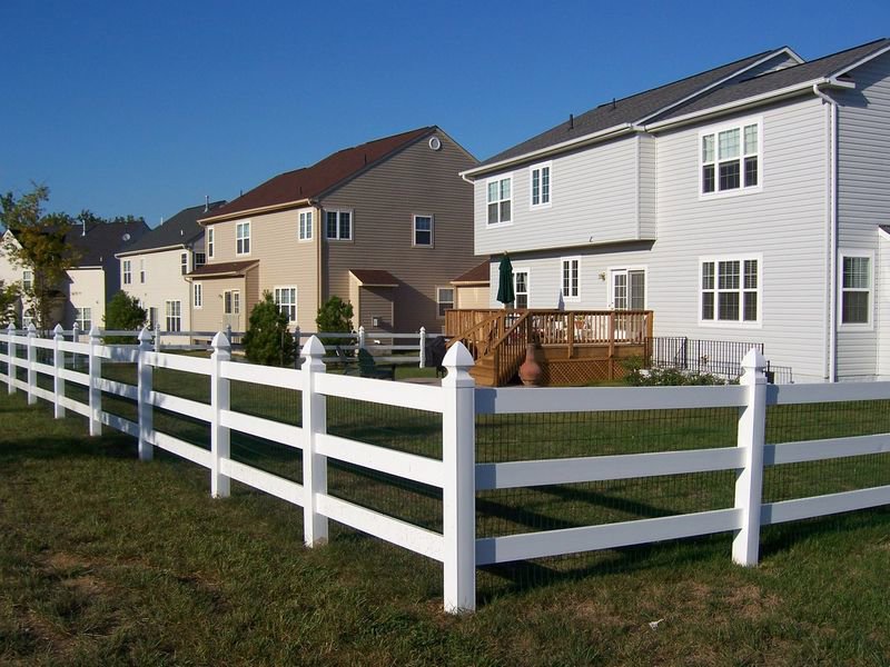 A white vinyl split-rail fence with wire mesh installed in a residential backyard by Crompton Fence Company in Charleston, SC.