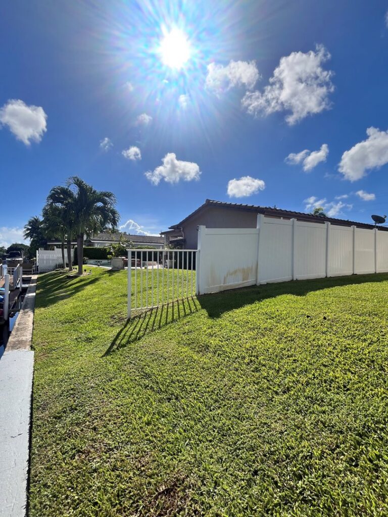 A white vinyl fence installed along a sunny waterfront property by Ace Fence Company in Fort Lauderdale, FL.