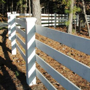 A white painted wooden post-and-rail fence installed in a wooded area by United Fence Company in Johnston, RI.