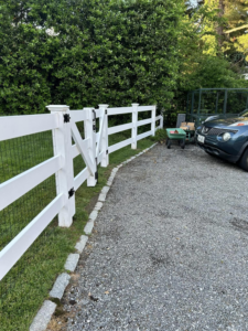 A white wood and wire mesh fence with a gate alongside a gravel driveway by Building Fences in Westchester NY.
