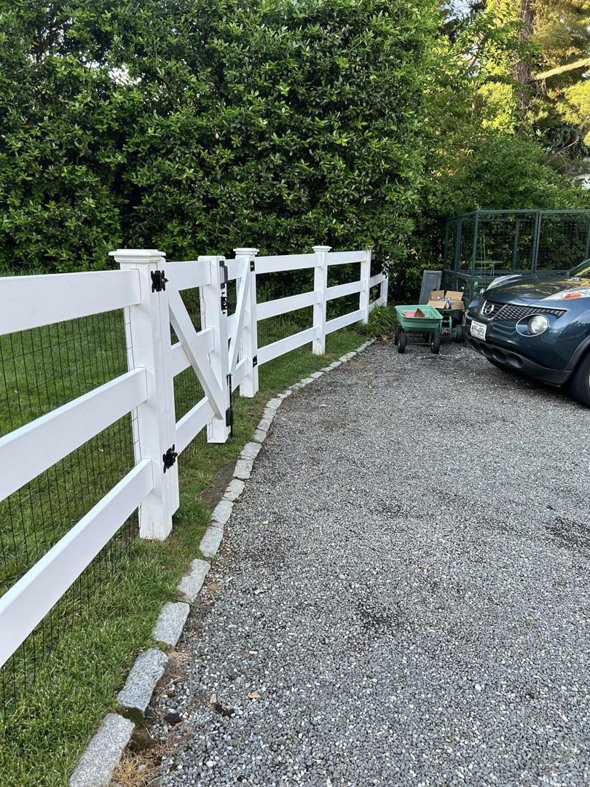 A white wood and wire mesh fence with a gate alongside a gravel driveway by Building Fences in Westchester NY.