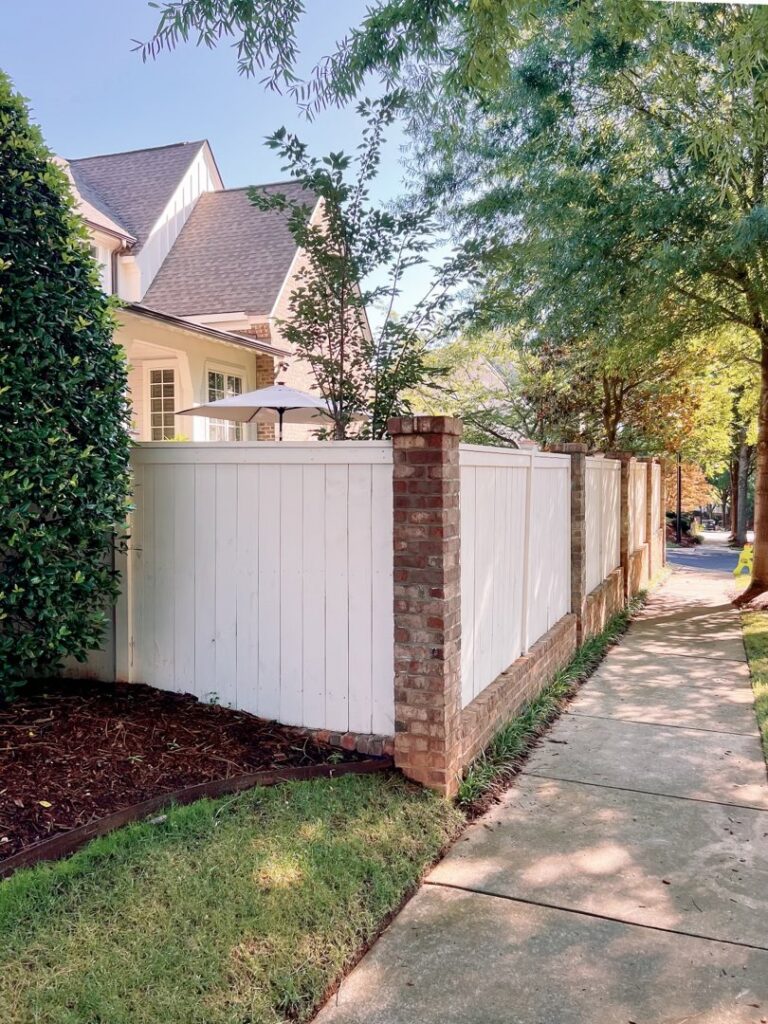 A white wooden fence with elegant brick pillars along a sidewalk by Heron Building Co in Franklin, TN.