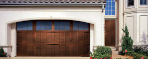 A house featuring a wide, dark wooden-style garage door with top windows by Overhead Door Company of Knoxville in Knoxville, TN