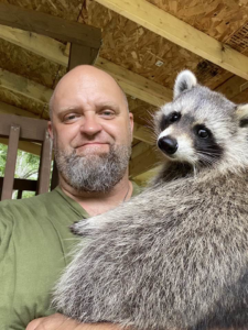 A wildlife control technician holding a raccoon at Rays Property maintenance and Pest Control in Churchville, NY