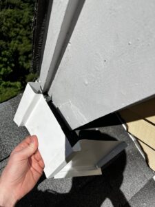 A technician holding a white metal vent cover, used for wildlife exclusion, near a roofline for Defense Pest and Wildlife Control in Hartford, CT.