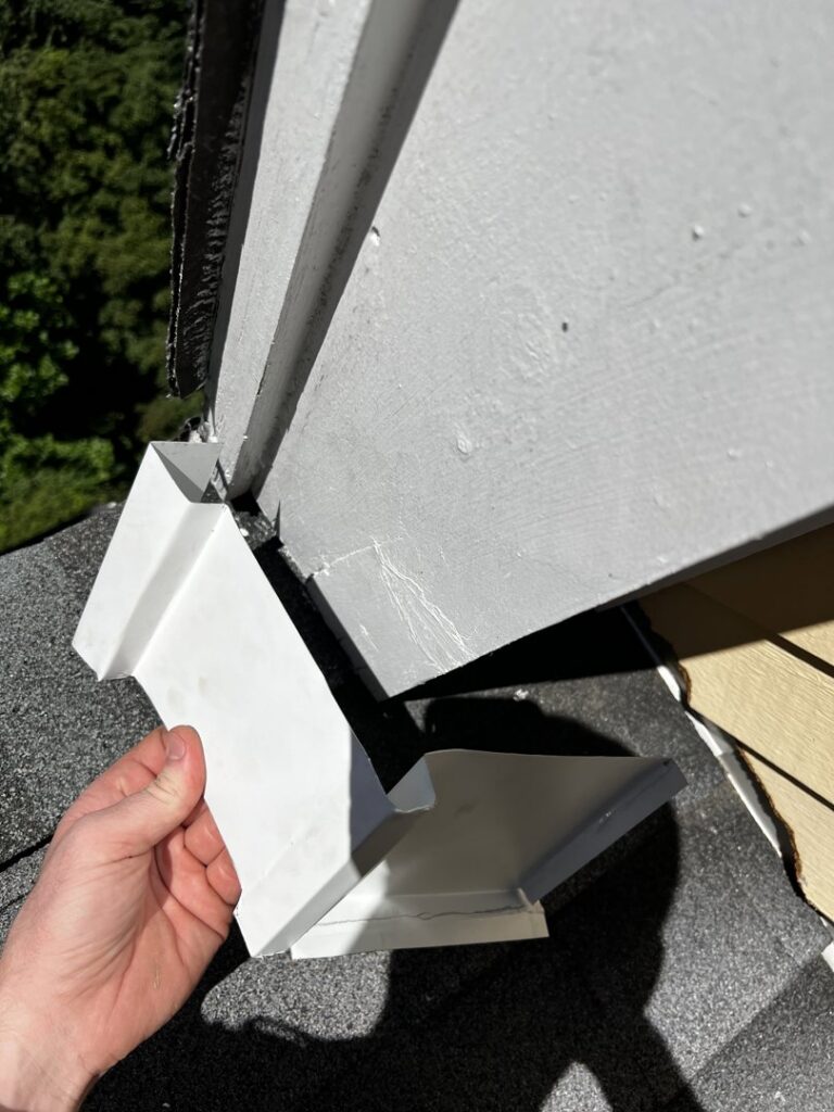 A technician holding a white metal vent cover, used for wildlife exclusion, near a roofline for Defense Pest and Wildlife Control in Hartford, CT.