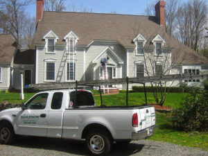 A Wildlife Extractors truck parked at a residential home with a worker on a ladder, performing wildlife control in Bridgewater, MA.