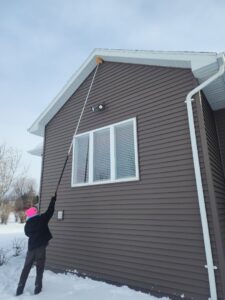 A Pest Badger technician performing winter pest control, removing webs from a house exterior in Chippewa Falls, WI.