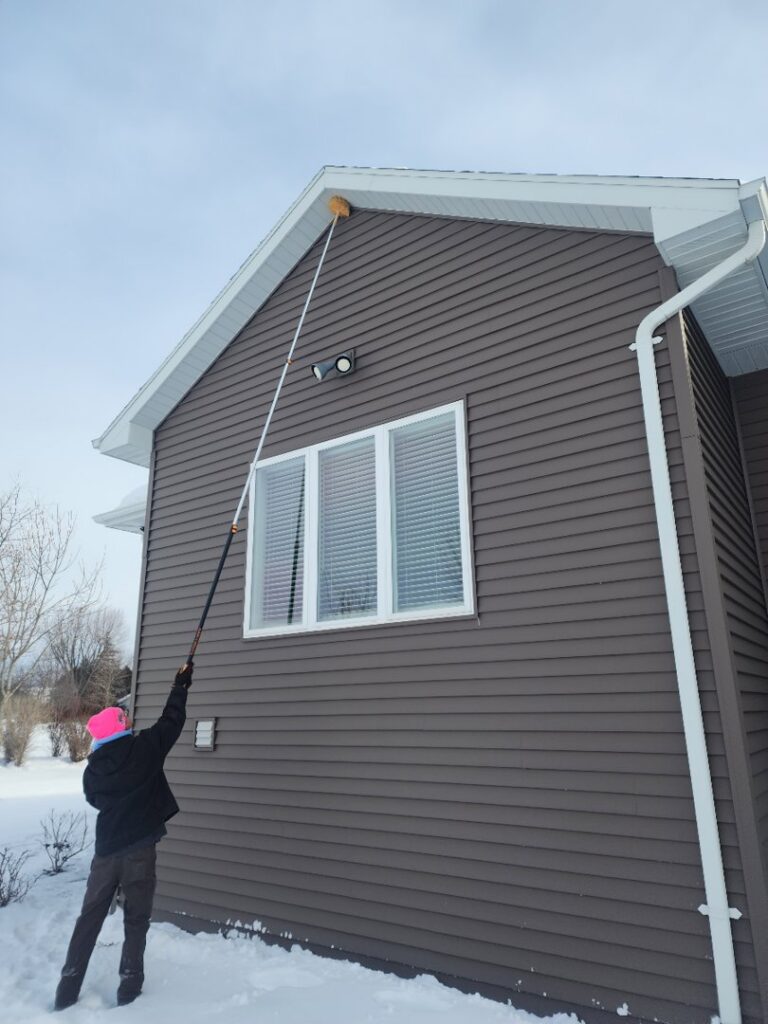 A Pest Badger technician performing winter pest control, removing webs from a house exterior in Chippewa Falls, WI.