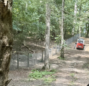 Wire fence installation in a wooded area with a Bobcat machine by Smith Land and Farm in Mansfield, GA