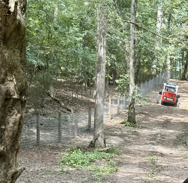 Wire fence installation in a wooded area with a Bobcat machine by Smith Land and Farm in Mansfield, GA