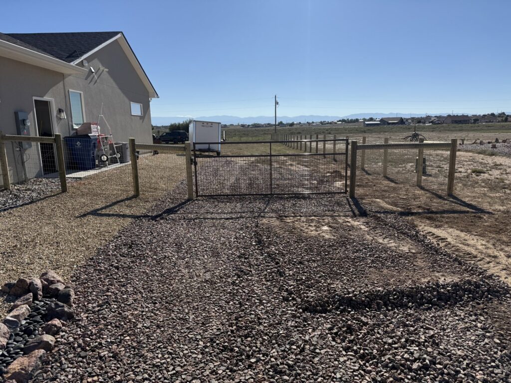 A wire fence with a black metal gate and gravel driveway by Pueblo Fence Co in Pueblo West, CO.