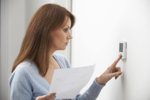 A woman adjusting a digital thermostat, showcasing home comfort services by Pioneer Heating and Cooling in Kalispell, MT