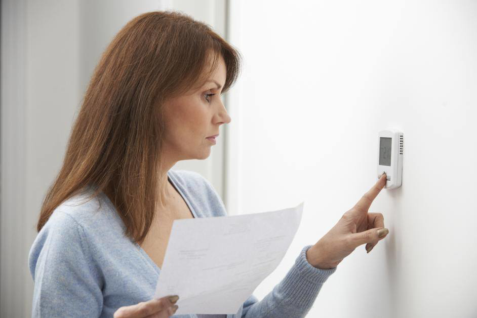 A woman adjusting a digital thermostat, showcasing home comfort services by Pioneer Heating and Cooling in Kalispell, MT