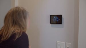 A woman adjusting a smart thermostat, representing HVAC control services by All Comfort Services in Madison, WI