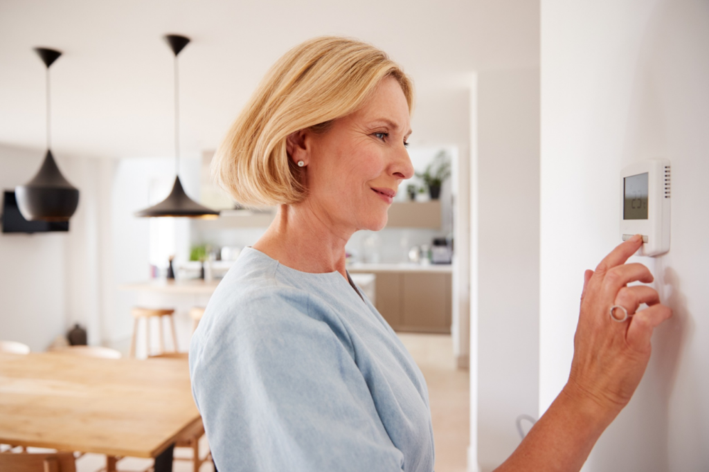 A woman adjusting a smart thermostat in her home, representing comfort provided by Cool Runnings HVAC LLC in Salisbury, MD.