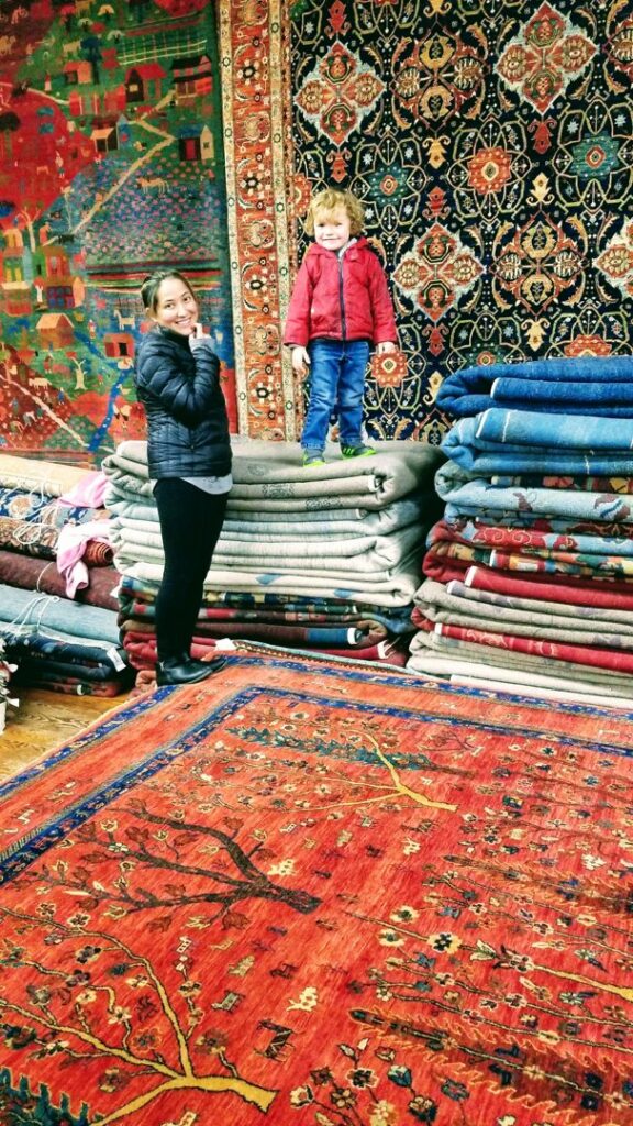 A woman and child exploring the diverse collection of tribal rugs in the showroom of Yayla Tribal Rugs, Inc. in Cambridge, MA.