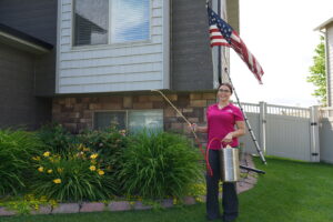 A woman from Eagle Eye Extermination spraying the exterior of a house for pest control in Kalispell, MT.