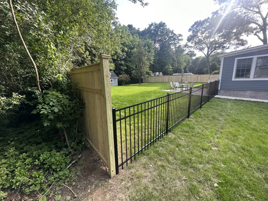 A combination of wooden privacy fence and black aluminum fence in a residential backyard by Quality Fence Inc. in Peekskill, NY