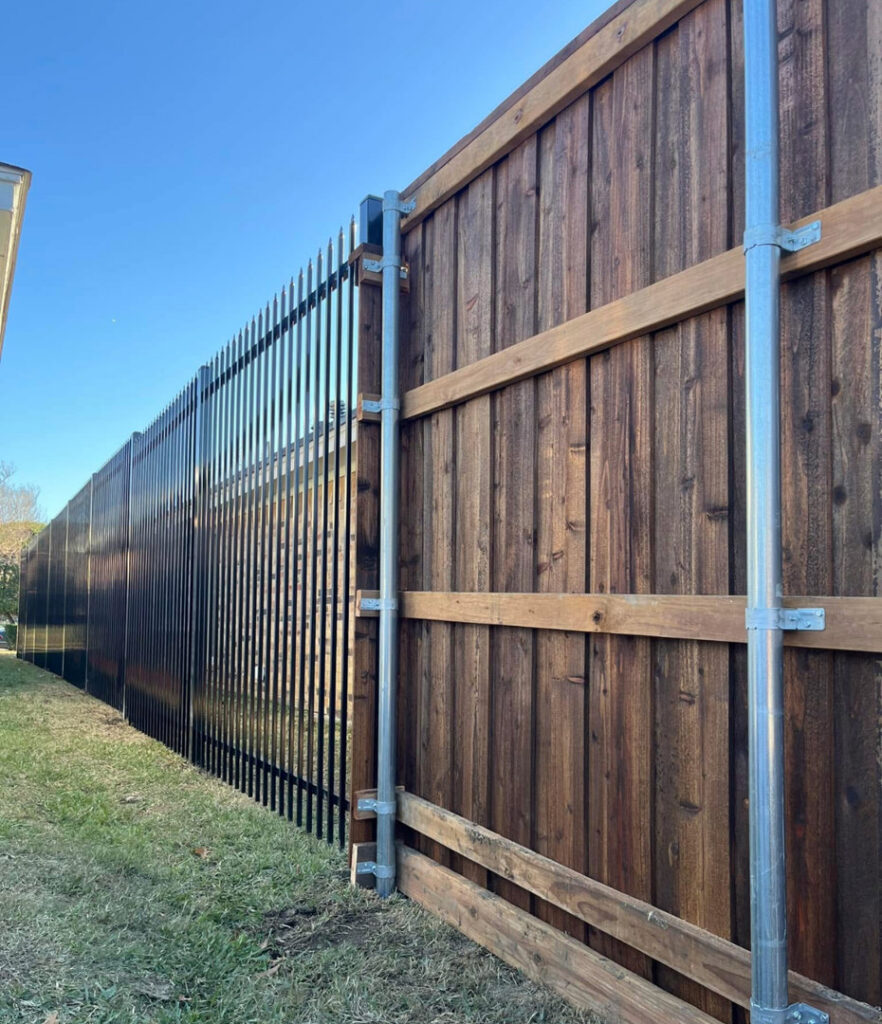 A custom fence combining dark stained wood panels and black metal pickets by Southern Fencing, LLC in Houma, LA.