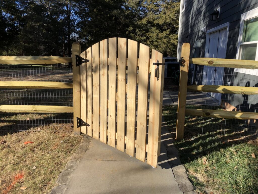 A newly installed wood arched gate with wire mesh and split-rail style fencing by Fenceitforu LLC in Matthews, NC.