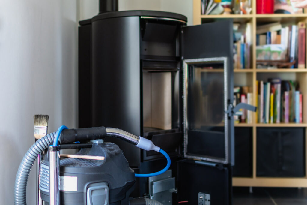 A wood-burning stove being cleaned with a vacuum, indicating a chimney sweep service by Top Chimney Fix in Denver, CO.