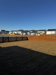 A residential backyard view with a wood fence in the foreground and a pond in the distance, installed by Stain and Go in Summerville, SC.