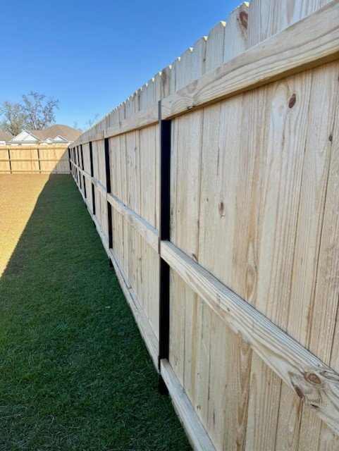 A newly installed wooden fence with black metal posts defining a residential property line by JBunlimitedfencingllc in Savannah, GA.