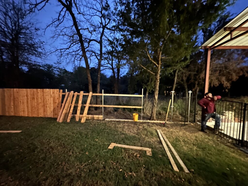 A wood fence under construction with panels stacked and posts in place at dusk, handled by NTX-Exterior Services in Dallas, TX.