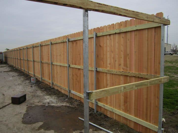 A long wooden fence under construction with metal posts and wood rails by Freedom Fencing of Clarksville, TN.