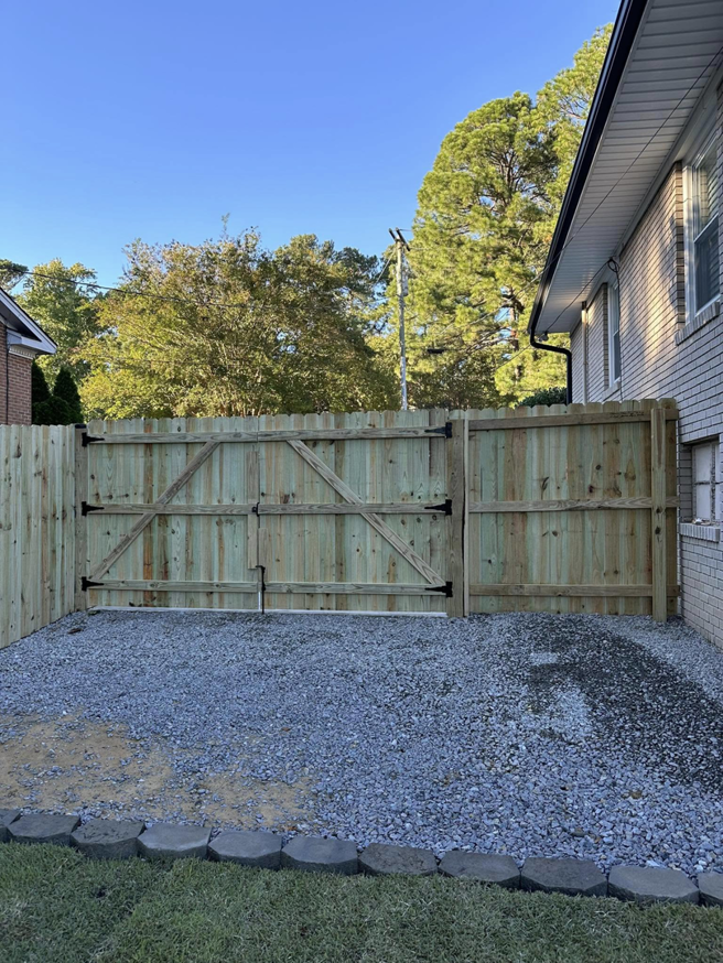 A newly installed wood fence gate and section of fence next to a house by First in Fencing and Remodeling in Fayetteville, NC.