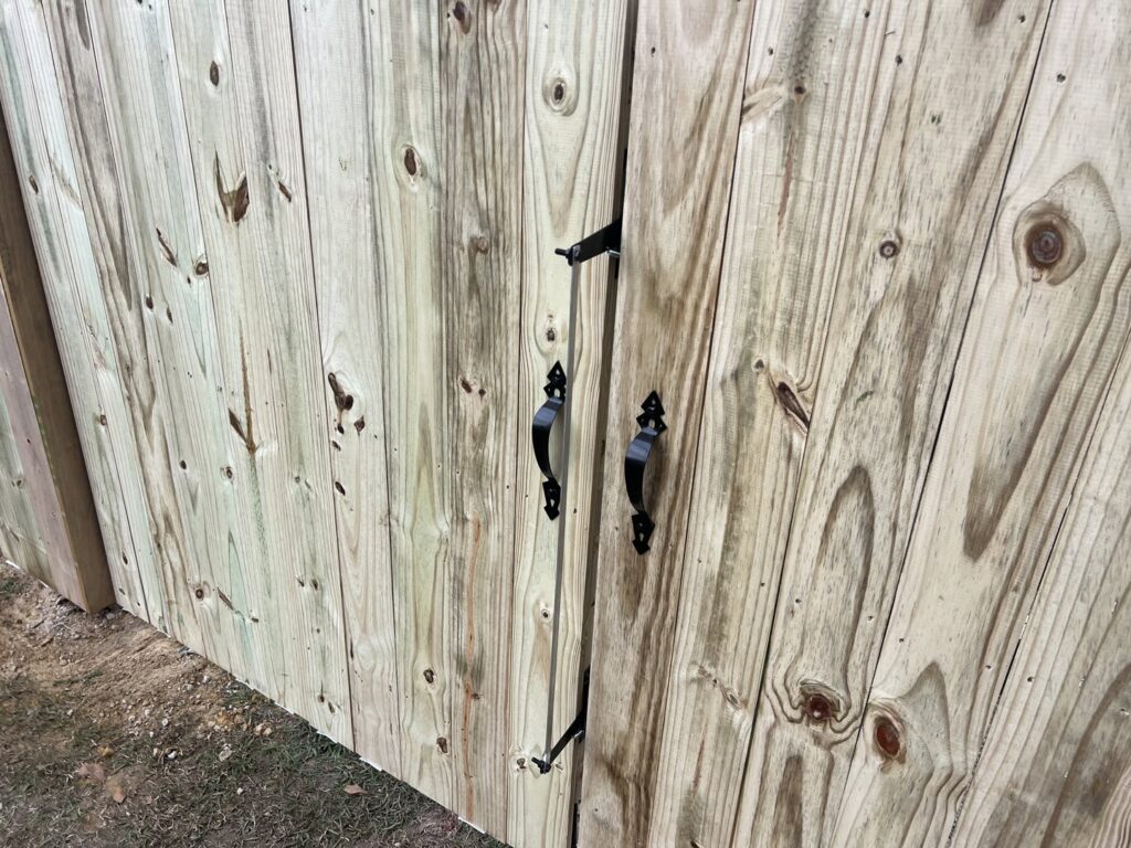 A close-up view of a wooden fence gate with black decorative handles and latch by Fencingphd.nc in Fayetteville, NC.