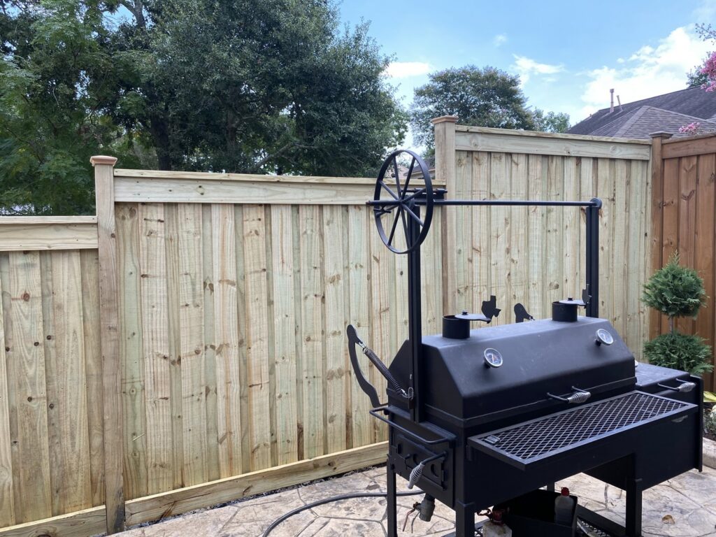 A new wood fence installation in a backyard with a large BBQ smoker, completed by Wood Fence Houston in Houston, TX.