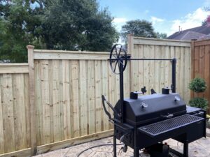 A new wood fence installation in a backyard with a large BBQ smoker, completed by Wood Fence Houston in Houston, TX.