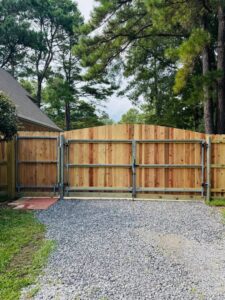 A sturdy wooden fence with a metal frame gate installed on a gravel driveway by Capitol Fencing in Baton Rouge, LA.