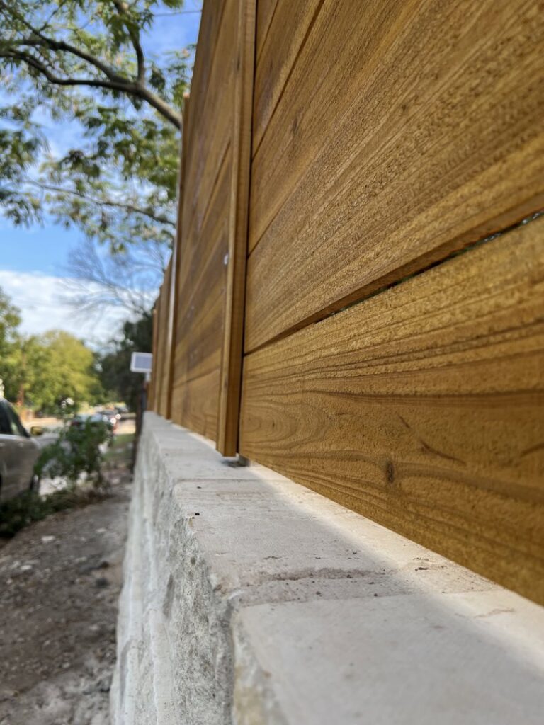 A new wooden fence installed on top of a stone wall by Good Neighbor Fencing and Construction in Austin, TX.