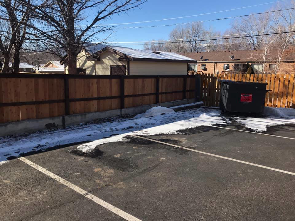 A long wood fence with a concrete base next to a parking lot, installed by Red Dirt Fencing and Woodwork, LLC in Fountain, CO.