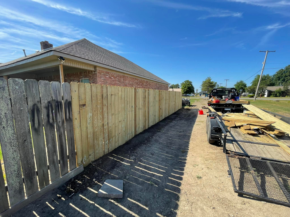 New wood fence installation replacing an older fence, with materials on a trailer, by Swanson Fencing in Jonesboro, AR.