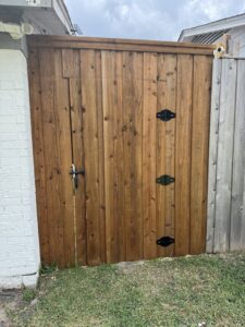 A custom wood gate with black hinges and latch installed next to a brick wall by Franco Fence in Garland, TX.