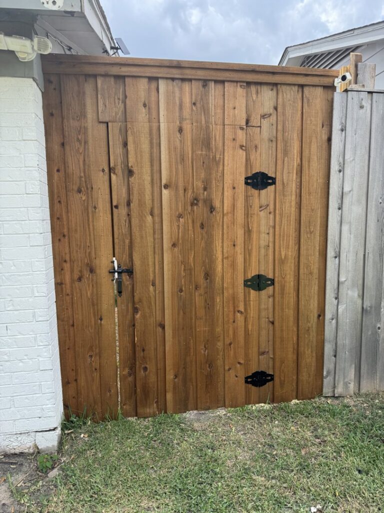 A custom wood gate with black hinges and latch installed next to a brick wall by Franco Fence in Garland, TX.