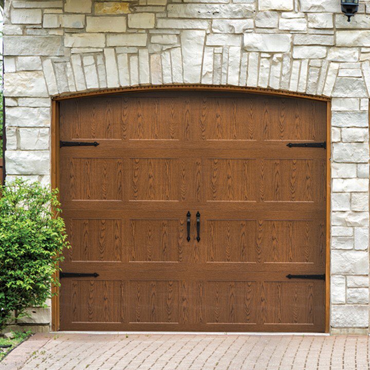 A beautiful wood-grain garage door with decorative hardware under a stone arch by American Overhead Door in Madison, AL
