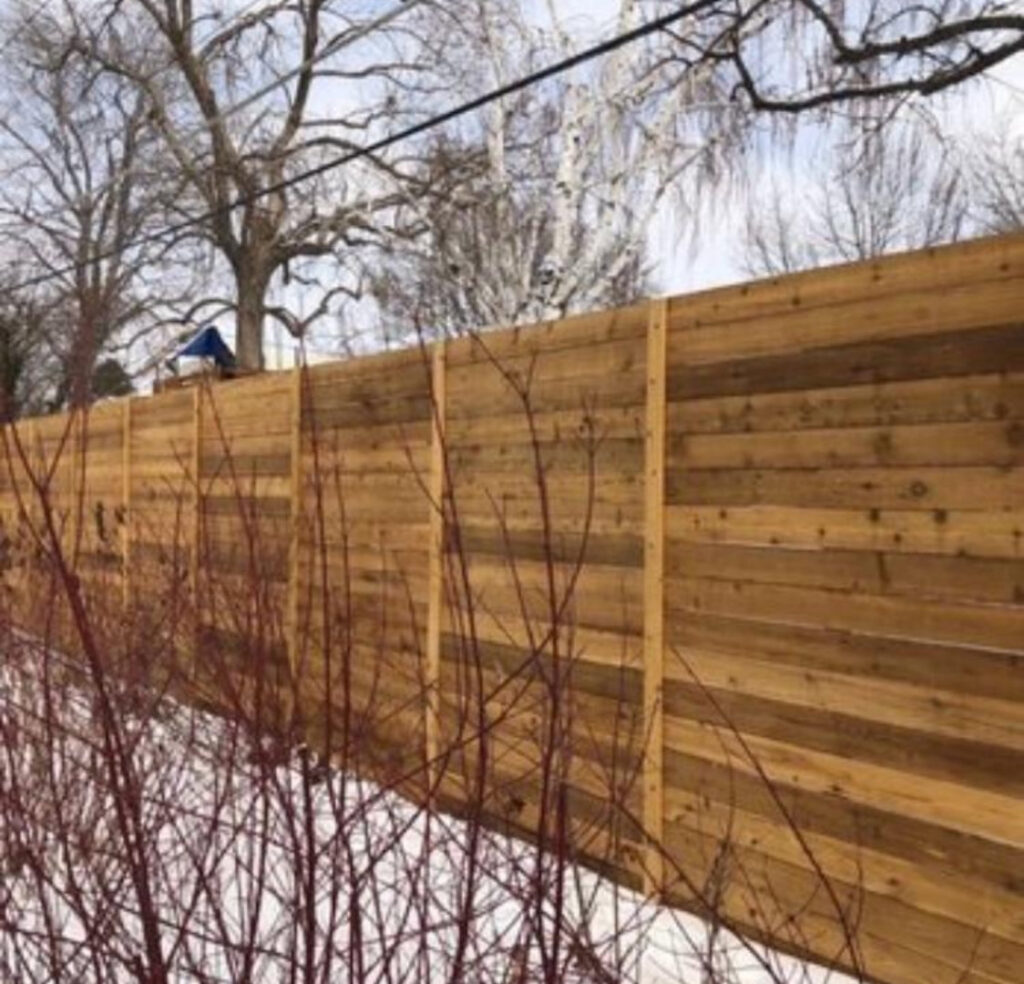 A wooden horizontal slat fence standing in a winter landscape, installed by R&S Fencing & Design LLC in Denver, CO.