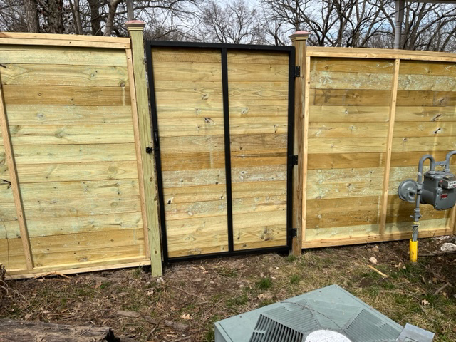 A new wood horizontal slat fence with a gate featuring a black metal frame by Fence Solutions of NWA in Gravette, AR.